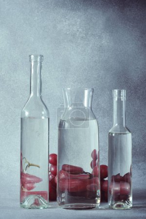 Téléchargez les photos : Nature morte des raisins vus à travers l'eau dans des bouteilles en verre clair - en image libre de droit