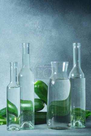 Téléchargez les photos : Bouteilles d'eau en verre et courgettes vertes sur une surface grise texturée - en image libre de droit