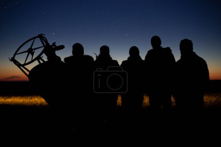 Umrisse im Schatten mehrerer Menschen im Gegenlicht mit einem Teleskop vor dem Hintergrund eines blauen Himmels mit Sternen