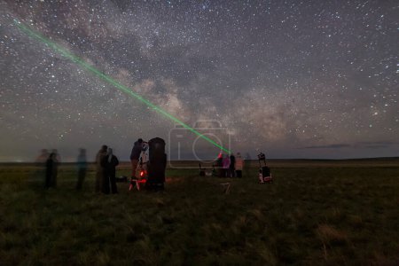 Nachts gibt es viele Teleskope auf dem astronomischen Beobachtungsort auf grünem Gras vor dem Hintergrund der Milchstraße und Sterne mit grünem Laserpointer. Langzeitbelichtungsastrofotografie