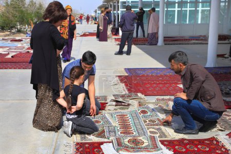 Téléchargez les photos : Achgabat, Turkménistan - Mart 15.2022 : Les gens achètent un tapis traditionnel turkmène fait à la main au bazar oriental. - en image libre de droit