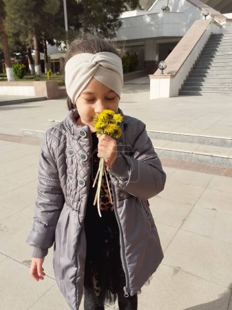 Téléchargez les photos : Achgabat, Turkménistan, Mart, 22 2022 : La fille renifle un bouquet de fleurs de pissenlit de printemps. - en image libre de droit