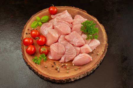 Rohe Stücke von Putenfleisch mit Kräutern und Tomaten auf einem Holzbrett auf schwarzem Hintergrund. Ogranes Essen und gesunde Ernährung. Hühnerfilet.Frische Stücke von Putenfleisch.Rohe Hühner.Nahaufnahme.