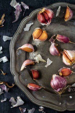 Raw garlic on grey pewter plate. Flat lay. Top view. Food concept. Dark mood food photography.