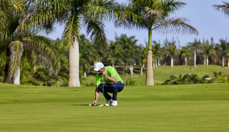 Golfista en el green con un putter en sus manos. Un jugador en el green evalúa las pendientes y la distancia desde el agujero antes de apuntar la pelota hacia la bandera.