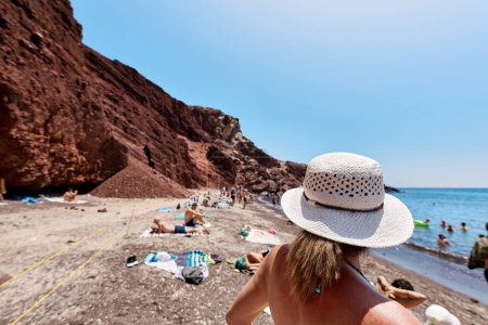 Femme au chapeau blanc observe la plage rouge (Kokkini Paralia). Îles Grecques, Santorin, Tourisme, Voyager