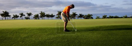 The golfer practices on the putting green with a golf iron, at first light in the morning.