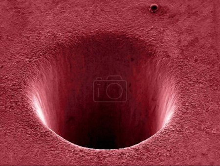 Foto de Cráter metálico formado por un láser. Micrógrafo electrónico de barrido coloreado (SEM) de un cráter a nanoescala formado en una superficie metálica por un haz láser de picosecod. - Imagen libre de derechos