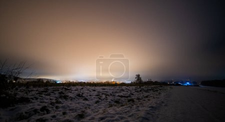 Photo for Night landscape of snowy field and a city with lights on the horizon. - Royalty Free Image