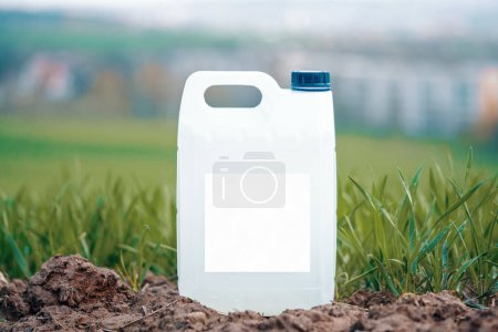 Téléchargez les photos : Conteneur en plastique blanc avec des produits chimiques agricoles ou des engrais sur un champ vert avec une étiquette vide. - en image libre de droit