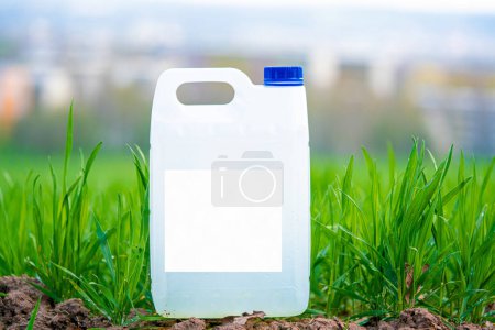 Foto de Recipiente de plástico blanco con productos químicos agrícolas o fertilizantes en un campo verde con una etiqueta vacía. - Imagen libre de derechos