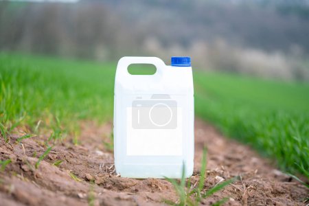 Téléchargez les photos : Conteneur en plastique blanc avec des produits chimiques agricoles ou des engrais sur un champ vert avec une étiquette vide. - en image libre de droit