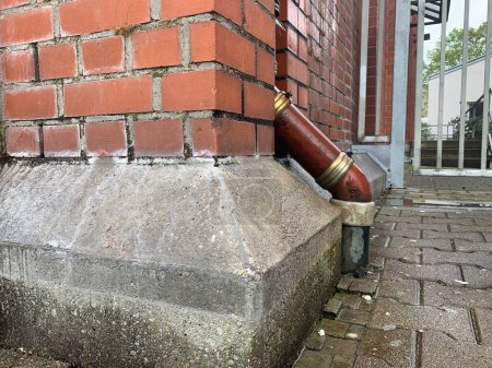 Una tubería de drenaje marrón que entra en el suelo sobre el fondo de una pared de ladrillo marrón en Alemania, la ciudad de Ludwigsburg. Al estilo de la vieja América. Vista lateral.