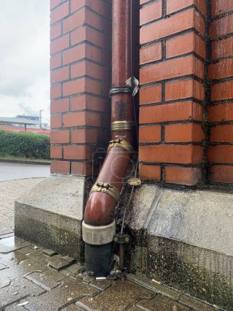 A brown drainpipe going into the ground against the background of a brown brick wall in Germany, the city of Ludwigsburg. In the style of old America. Side view, front.