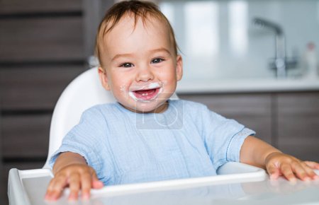 Foto de Bebé sonriente comiendo comida en la cocina. Nutrición infantil. - Imagen libre de derechos