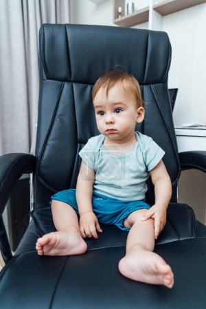 Photo for A baby boy sitting in a big black leather chair. Little baby boss. - Royalty Free Image