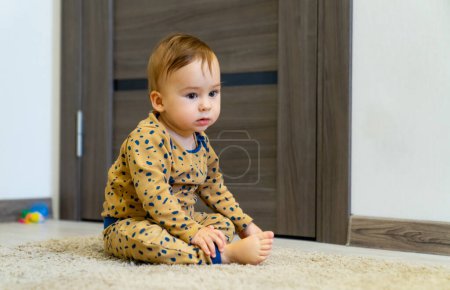 Foto de Cute little boy is playing with toys while sitting on floor. Curious baby boy studying nursery room. - Imagen libre de derechos