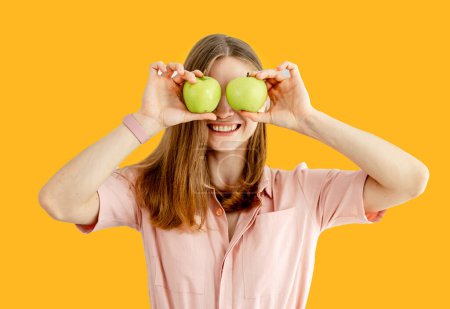 Photo for Woman ready to prepare meal with vegetables and fruits. Woman is holding apples near her eyes. Isolated on yellow background - Royalty Free Image