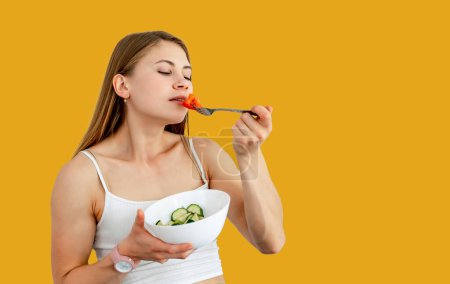 Attractive woman smelling cut tomato on fork isolated on yellow studio wall. Blurred background. Healthy food and lifestyle concept. Closeup.