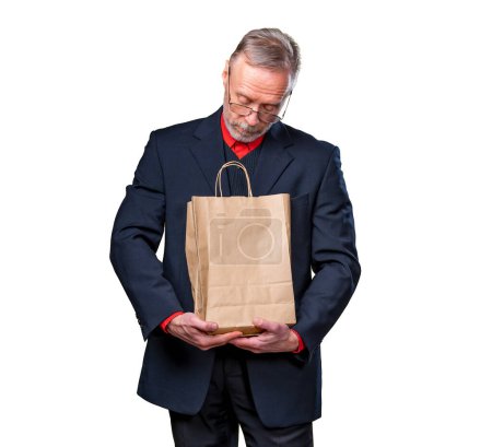 Foto de Man looks at a paper bag receiving a present isolated on a white background. Eco shopping. Man in suit - Imagen libre de derechos