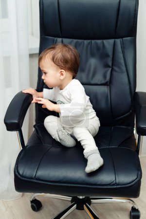 Infant child sitting on office chair. Adorable boy sitting on business chair.