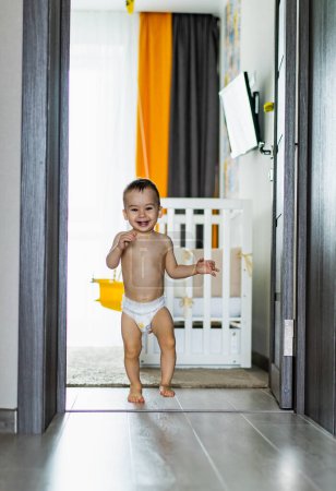 Téléchargez les photos : Bébé mignon debout dans une porte portant une couche. Un bébé dans une couche debout dans une porte - en image libre de droit