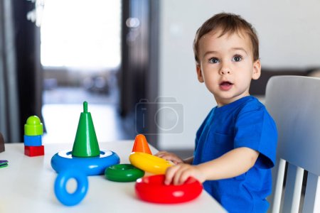 Téléchargez les photos : Jeune enfant engagé dans un jeu imaginatif à une table remplie de jouets. Un petit garçon assis à une table jouant avec des jouets - en image libre de droit