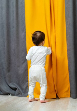 Téléchargez les photos : Curieux enfant debout devant un rideau coloré. Un petit enfant debout devant un rideau - en image libre de droit