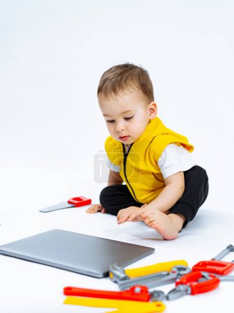 Téléchargez les photos : Bébé jouant avec des outils sur le sol. Un bébé assis sur le sol jouant avec des outils - en image libre de droit