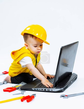 Photo for Young child wearing a hard hat and using a laptop for educational play. A small child wearing a hard hat and using a laptop - Royalty Free Image