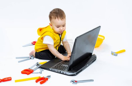 Téléchargez les photos : Jeune garçon utilisant un ordinateur portable assis sur le sol. Un petit garçon assis sur le sol avec un ordinateur portable - en image libre de droit