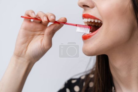 A woman brushing her teeth with a red toothbrush. A Woman Engaging in Oral Hygiene with a Vibrant Red Toothbrush