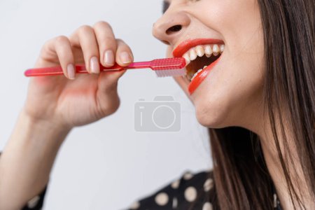 Téléchargez les photos : Une femme se brosse les dents avec une brosse à dents rose. Une femme qui s'engage dans l'hygiène buccale avec une brosse à dents aux couleurs vives - en image libre de droit