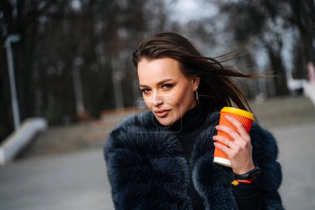 A woman in a fur coat holding a cup of coffee. A Stylish Woman Enjoying a Warm Cup of Coffee in Her Luxurious Fur Coat