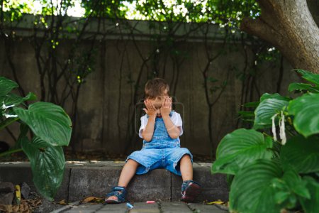 Foto de A Young Boy Finding Solace on a Stone Bench, Abracing Reflection and Privacy (en inglés). Un joven sentado en un banco de piedra cubriéndose la cara - Imagen libre de derechos