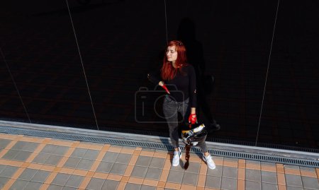 Téléchargez les photos : Une femme debout sur un trottoir tenant une planche à roulettes. Une femme debout sur un trottoir tenant un skateboard - en image libre de droit