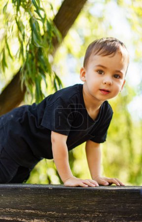 Téléchargez les photos : Un jeune garçon curieux scrutant une clôture en bois rustique. Un jeune garçon penché sur un rail en bois - en image libre de droit