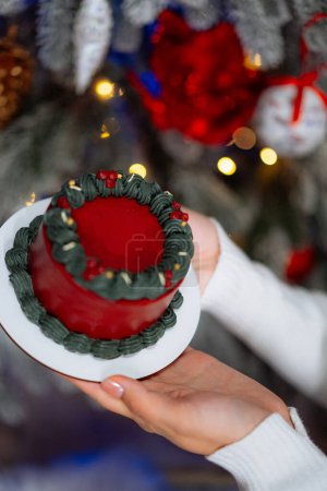 Téléchargez les photos : Une personne présente joyeusement un gâteau rouge et vert vibrant devant un arbre de Noël magnifiquement orné. - en image libre de droit