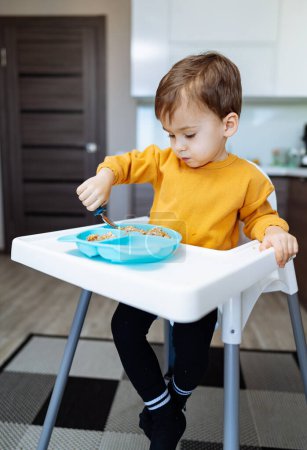 Téléchargez les photos : Un petit garçon se livre à une délicieuse exploration culinaire, perché dans sa chaise haute, savourant chaque bouchée de nourriture. - en image libre de droit