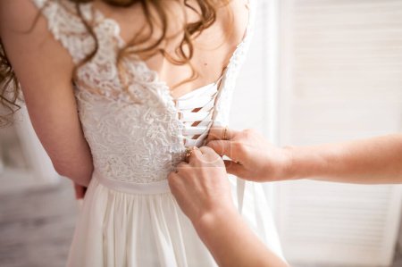 Téléchargez les photos : Une fée bienveillante aide amoureusement la mariée alors qu'elle perfectionne sa robe de mariée avant la cérémonie magique. - en image libre de droit