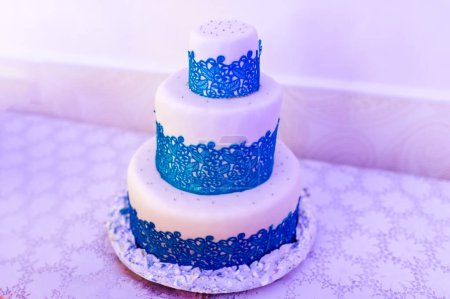 Téléchargez les photos : Une œuvre d'art fabriquée à partir de sucre, glaçage et rêves, un gâteau fantaisiste à trois niveaux prend le devant de la scène sur une charmante table. - en image libre de droit