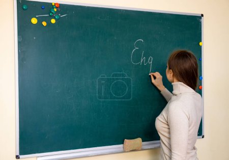 Téléchargez les photos : Une femme se tient devant un tableau noir dans une salle de classe, enseignant et écrivant des informations importantes pour ses élèves. - en image libre de droit