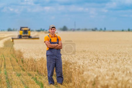 Téléchargez les photos : Fermier se tient dans le champ de blé avec moissonneuse-batteuse dans le backg - en image libre de droit