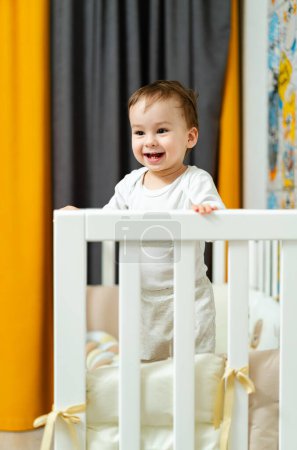 Téléchargez les photos : A baby is standing in front of a crib with a white shirt that says I love you on it - en image libre de droit