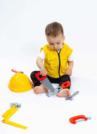 Téléchargez les photos : A young boy is playing with a toy set that includes a hammer, a saw, and a wrench - en image libre de droit