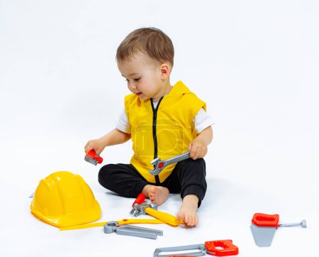 Téléchargez les photos : A young child is playing with a toy set that includes a yellow hard hat and a wrench. The child is sitting on the floor and he is enjoying the activity - en image libre de droit