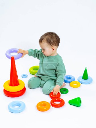 Téléchargez les photos : Un bébé joue avec une pile d'anneaux en plastique coloré. Les anneaux sont disposés en forme de pyramide - en image libre de droit