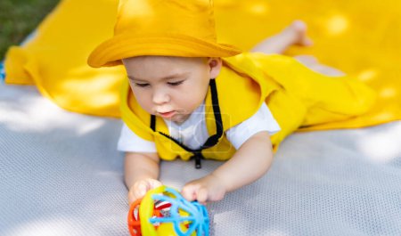 Téléchargez les photos : Un bébé est allongé sur une couverture et tient un jouet. Le bébé porte un chapeau jaune et une tenue jaune - en image libre de droit