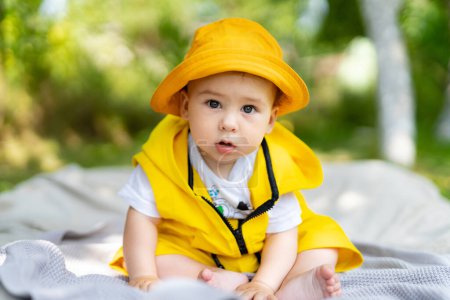 Téléchargez les photos : Un bébé portant un imperméable jaune et un chapeau est assis sur une couverture - en image libre de droit