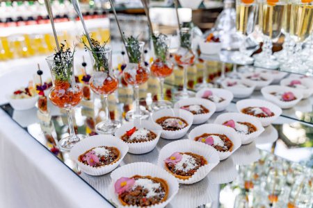 Téléchargez les photos : Une table avec une variété d'entrées et de desserts, y compris un plateau de mini tartes avec des fleurs roses sur le dessus - en image libre de droit